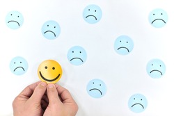 A smiling face icon among a group of sad emoticons in white background. Be positive and stay happy concept.