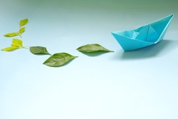 Clean energy for sea and cargo transportation and travel and sustainable maritime transport concept. Paper boat emitting fresh green leaves. 