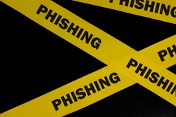 Phishing scam alert, caution and warning concept. Yellow barricade tape with word phishing in dark black background.