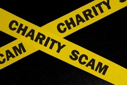 Charity and donation scam and fraud alert, caution and warning concept. Yellow barricade tape with word in dark black background.