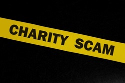 Charity and donation scam and fraud alert, caution and warning concept. Yellow barricade tape with word in dark black background.