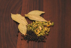Spices on a wooden background, close-up. Bay leaf, black pepper peas and cardamom. Seasonings and herbs of world cuisines