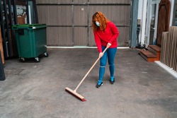 A female worker wearing a mask sweeping the garage with a large broom
