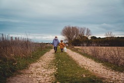 Wide shot of two boys with their backs holding a lantern walking down a country lane on a cloudy autumn day.