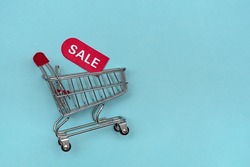 Mini cart with red coupon for discounts. The concept of sales and discounts of goods. On a blue background.