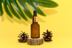 Cosmetic oil in a glass bottle stands on a wooden podium. Palm leaf on a yellow background. Close-up.