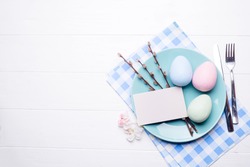 colored eggs on blue plate with flowers on white wooden background, flat lay