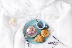 Breakfast in bed with tea, flower and croissant: teapot of flower tea with Fresh croissants on a plate . Valentine's day breakfast in bed, Mother's day or Women's day concept Flat lay