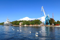 Large port crane for unloading ships in Baltiysk. Swans are swimming. Warship