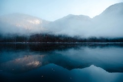 Morning winter fog over lake Konigsee in Berchtesgaden. Reflection on water surface of rocky bavarian alps. Dark mysterious atmosphere.