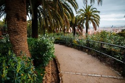 Walking path in green areas of Guell park with great landscape view to Barcelona city. Exotic palms and green bushes in famous tourists place in Spain.