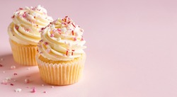 Vanilla cupcakes with cream cheese frosting and pink sprinkles on pink background. Saint Valentine's day or birthday dessert. Beautiful festive food for wedding or baby shower girl. Copy space.