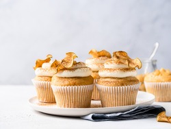 Apple cupcakes with cream cheese frosting decorated with dried apple slices and cinnamon powder. Autumn festive dessert. Homemade pastry on ceramic plate. Close up food. Copy space. Morning table.