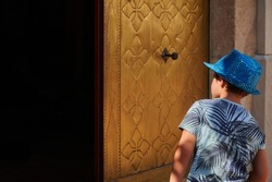 Kid in a blue cap peering into a dark place with a gold-colored door. Curiosity concept	