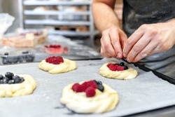 A close-up photograph capturing an anonymous bakery worker's skilled hands, meticulously filling pastries with red currants and raspberries before baking.