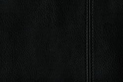 Texture of genuine black leather with a seam on the left side. Abstract monochrome background. A simple background of natural leather.