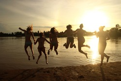 Silhouette of happy girls having fun in nature party, jumping to river in sunset in Si Phan Don, Laos