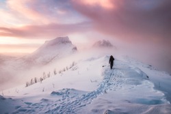 Man mountaineer walking with snow footprint on snow peak ridge in blizzard at morning