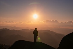Successful young hiker man standing on top of mountain with the sun in the sunset at national park