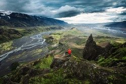 Dramatic view of Hiker man in red jacket standing on top of Valahnukur viewpoint surrounded by volcanic mountain and Krossa river in Icelandic Highlands at Thorsmork, Iceland