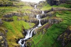 Beautiful Klifbrekkufossar seven tier waterfall flowing hidden in the Mjoifjordur Fjord on summer at East of Iceland
