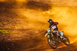 Motocross pilot in a turn during sunset with golden smoke on dirt track