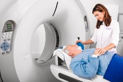 Radiographer reassuring senior man going into CT scanner in hospital