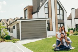 Family sitting on lawn in backyard, big modern house on background