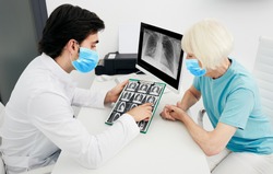Pulmonologist wearing a protective mask showing a senior patient a CT scan of her lungs. Pneumonia, coronavirus, lung disease