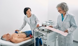 Cardiogram test. Elderly male patient receives heart rate monitored using electrocardiogram equipment with two doctors cardiologist