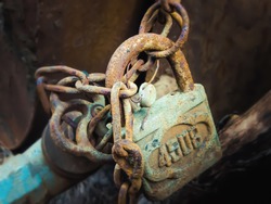 An old padlock on a chain blocking a pipe with a valve. Abandoned place with rusty objects. The number on the iron is 4508. The atmosphere of stalking, abandonment and mystery. Themes of horror.