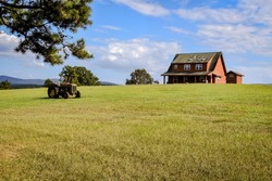 A country house on a hill with a old tractor sitting in front of it- A vintage tractor sitting in an open field on a country farm- a ranch with a old tractor sitting in the pasture- Old farm tractor 
