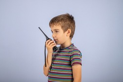 The boy is talking on the radio. A professional walkie-talkie in the child's hand. The child speaks into a walkie-talkie on a blue background. Boys' games.