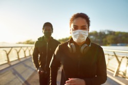 Jogging during quarantine. Young african couple wearing face medical masks while running together on the bridge in the morning. Sport and coronavirus. Covid-19. Protection. Social distancing