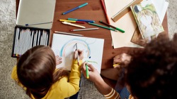 Top view of caucasian little girl spending time with african american baby sitter. They are drawing a mouse together. Children education, leisure activities, babysitting concept. Selective focus