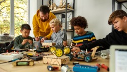 Young technicians building a robot, working with a wiring kit together with a male teacher at a stem robotics class. Inventions and creativity for kids. Selective focus. Web Banner