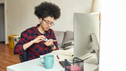 Young afro american woman using hand sanitizer, antiseptic gel while sitting at her workplace and working or studying online from home. Hygiene and Healthcare. Covid 19. Self isolation. Stay home