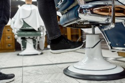 Cropped photo of adjustable barber chair. Barber adjusting barber chair while working in the modern barbershop. Selective focus, close up. Hair salon. Barbershop concept
