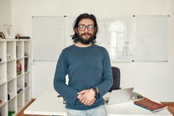 Giving online class. Portrait of young happy bearded male teacher wearing glasses standing against whiteboard and looking at camera. Focus on a man. E-learning. Distance education. Stay home