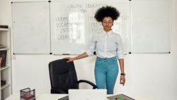 Portrait of young happy afro american woman, female teacher standing near whiteboard and looking at camera, teaching Spanish language online from home. E-learning. Distance education. Stay home