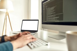 Cropped shot of male web developer writing code on desktop computer while sitting at his workplace and working from home, typing on keyboard. Focus on laptop. Working online. Stay home, self isolation