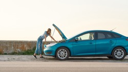 Full length shot of young woman looking under the hood of her broken car, trying to repair it on her own while standing alone after car breakdown on the road side, Side view, Web Banner