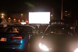 The best place to go. Many cars parked in front of a big white screen to watch movies or films sitting inside the car at drive in cinema in the evening. Entertainment, hobby concept
