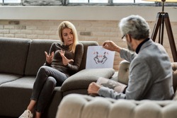 Young caucasian woman discussing Rorschach test pictures with psychotherapist during session in office, selective focus. Psychotherapy concept