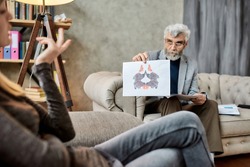 Psychotherapist showing Rorschach inkblot test pictures to young caucasian woman during session in office, selective focus. Psychotherapy concept