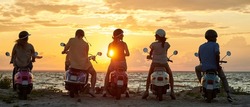 Group of young friends, motorcycle riders wearing helmets standing with their scooters on the coast, enjoying sunset. Friendship, leisure activity, summertime, relax concept. Rear view. Web Banner