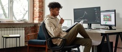 Narrow web banner view of pensive African American millennial gen z male trader read book work online on PC at home. Serious young ethnic man financial expert analyze graph chart. Cryptocurrency.