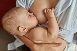 Mother breastfeeding her newborn baby boy holding him in cradle position. Perfect position for nursing to make process comfortable for both mother and child.