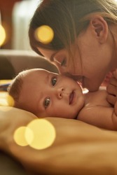 Lovely mother loves to smell her adorable baby. Sweet child lying on back, close up face. Mother leaning over her baby, sniffing its smell. Closeup portrait with bokeh balls.