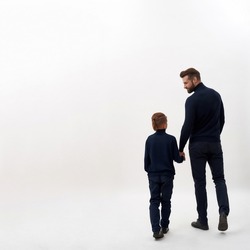 Back view of young father and small son hold hands walk together, isolated on white studio background. Loving dad lead little boy child kid in life, show support protection. Fatherhood concept.